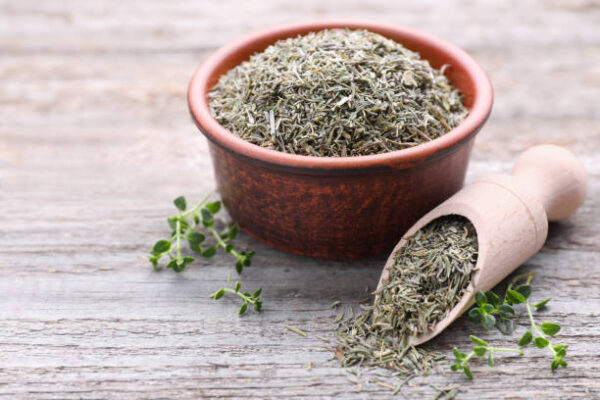 Bowl with scoop of dried and fresh thyme on wooden table, closeup